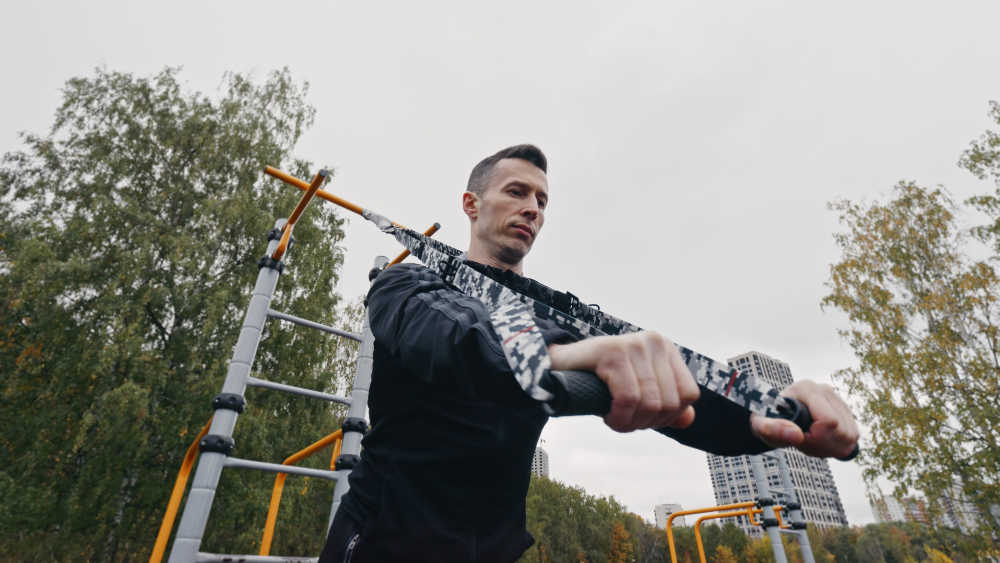 Андрей Карпиков, мастер-спорта делает упражнение на спортивной площадке с тренировочными петлями