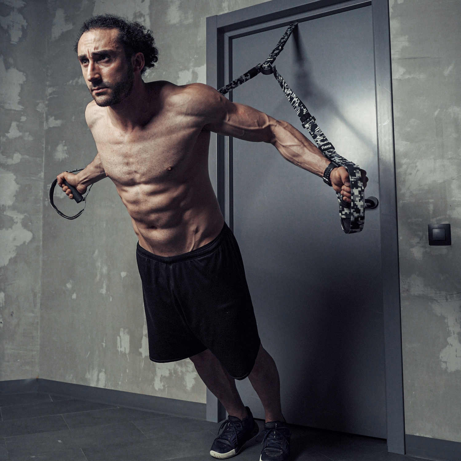 Мужчина в форме и с накаченным прессом делает упражнение на тренировочных петлях от двери