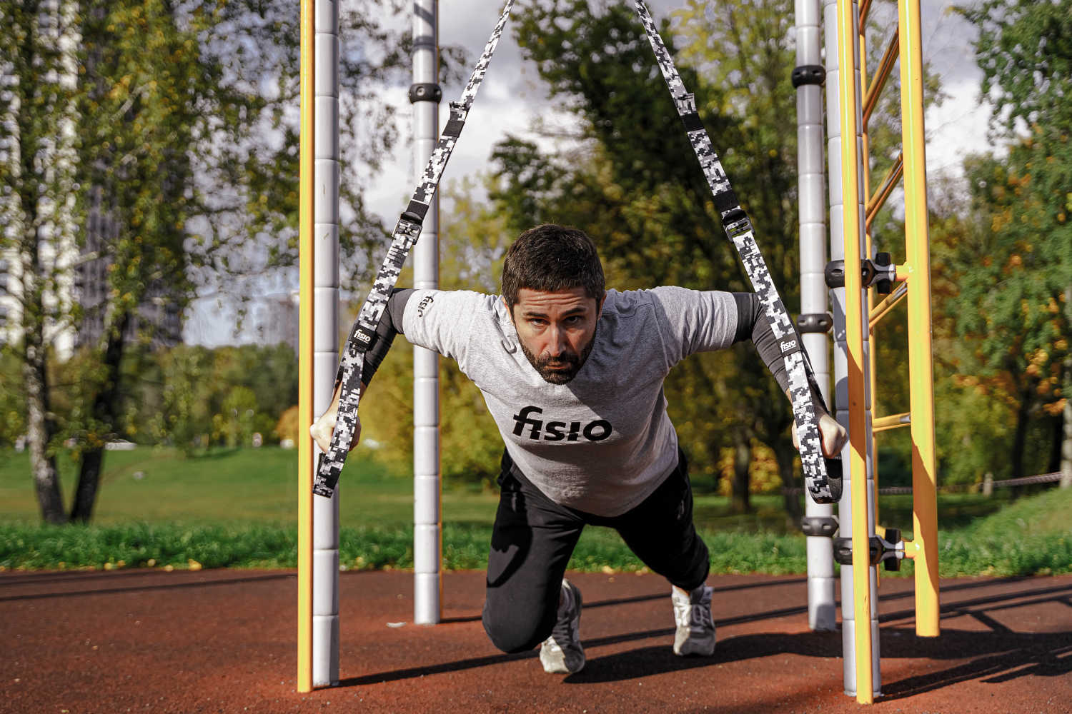 Привлекательный мужчина тренируется на спортивной площадке с функциональными петлями FISIO